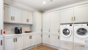 A modern kitchen with white cabinets, a coffee maker, and a washing machine. - Owen Glen Cottage Clifden (Clifden)