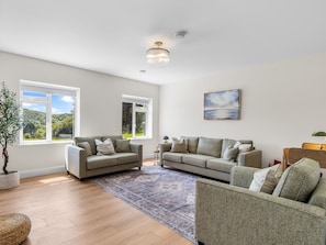 A spacious living room with two sofas, a coffee table, and a large window offering a view of greenery. - Owen Glen Cottage Modern Holiday Home Near Clifden Town (Clifden)