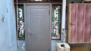 A grey door with a brass handle, a stone base, and a white plastic stool.