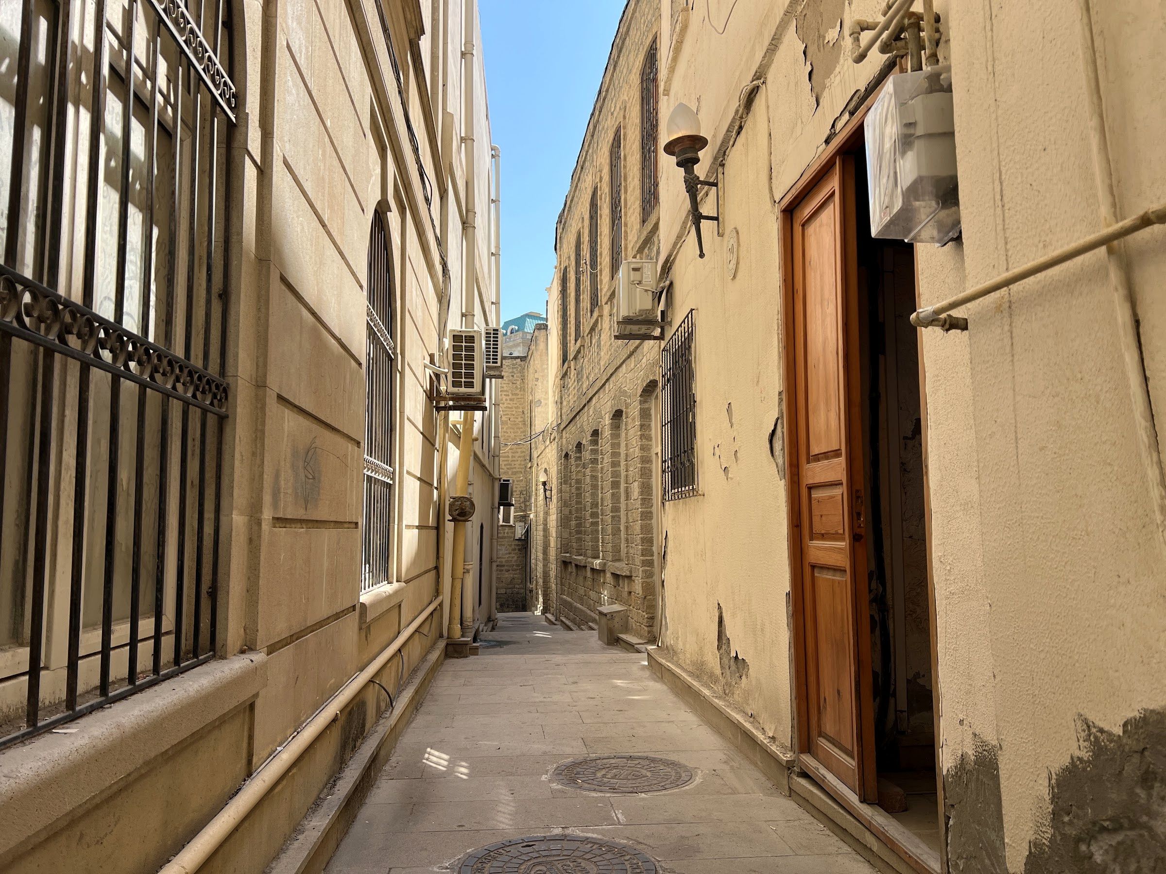 A narrow alleyway with buildings on either side, a metal gate, and a wooden door.