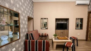 A living room with a sofa, a TV, a table with a chessboard, and a mirror.