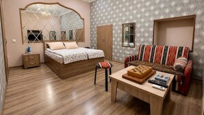 A bedroom with a bed, a wooden nightstand, a dresser, a mirror, a sofa, and a table with a chessboard and books.