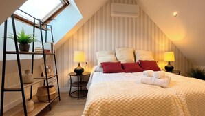 A bedroom with a sloped ceiling, a skylight, a bed with white bedding, red pillows, two bedside lamps, and a small plant on a shelf. - Las Posada de las Flores (Astorga)