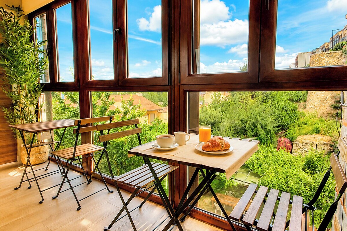 A balcony with a table set for breakfast, chairs, and a potted plant.