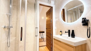 A modern bathroom with a shower, a sink with a mirror, and a telephone. - Las Posada de las Flores (Astorga)