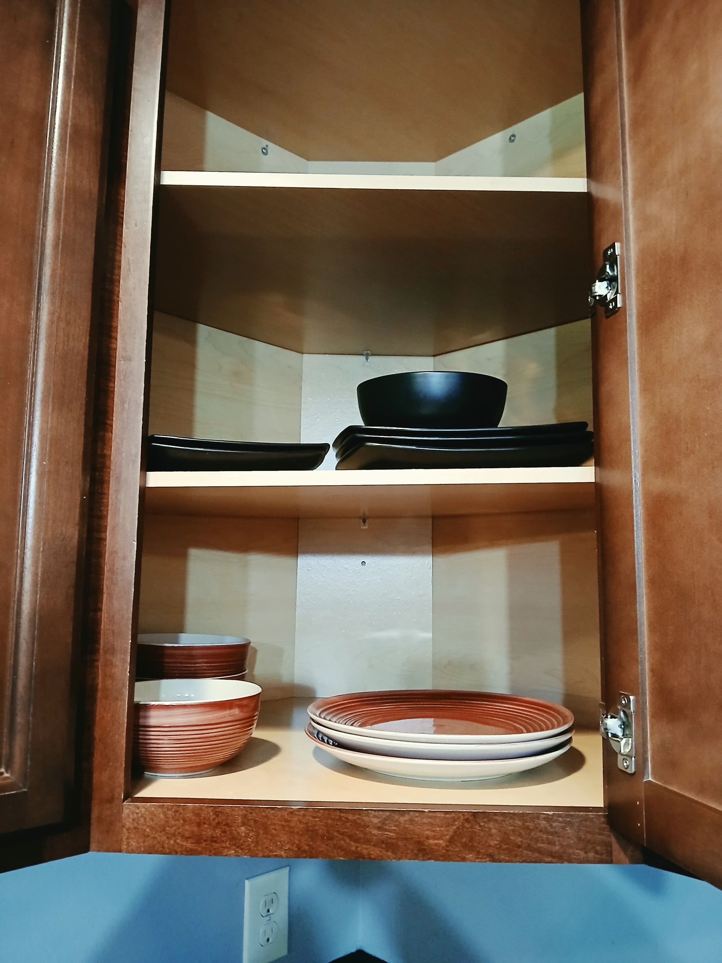 A wooden cabinet with three shelves, each holding different kitchenware.