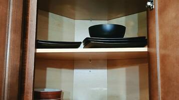 A wooden cabinet with three shelves, each holding different kitchenware.