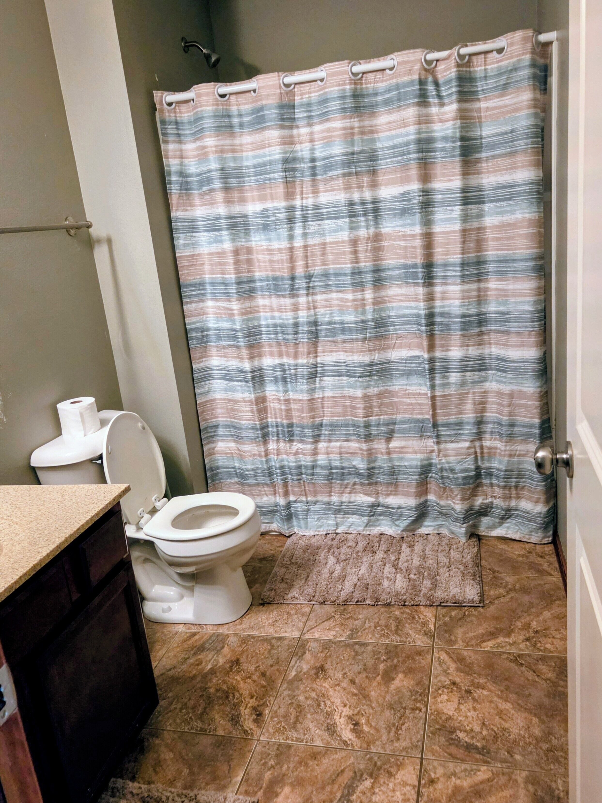 Ein Badezimmer mit Toilette, Duschvorhang und Fliesenboden.