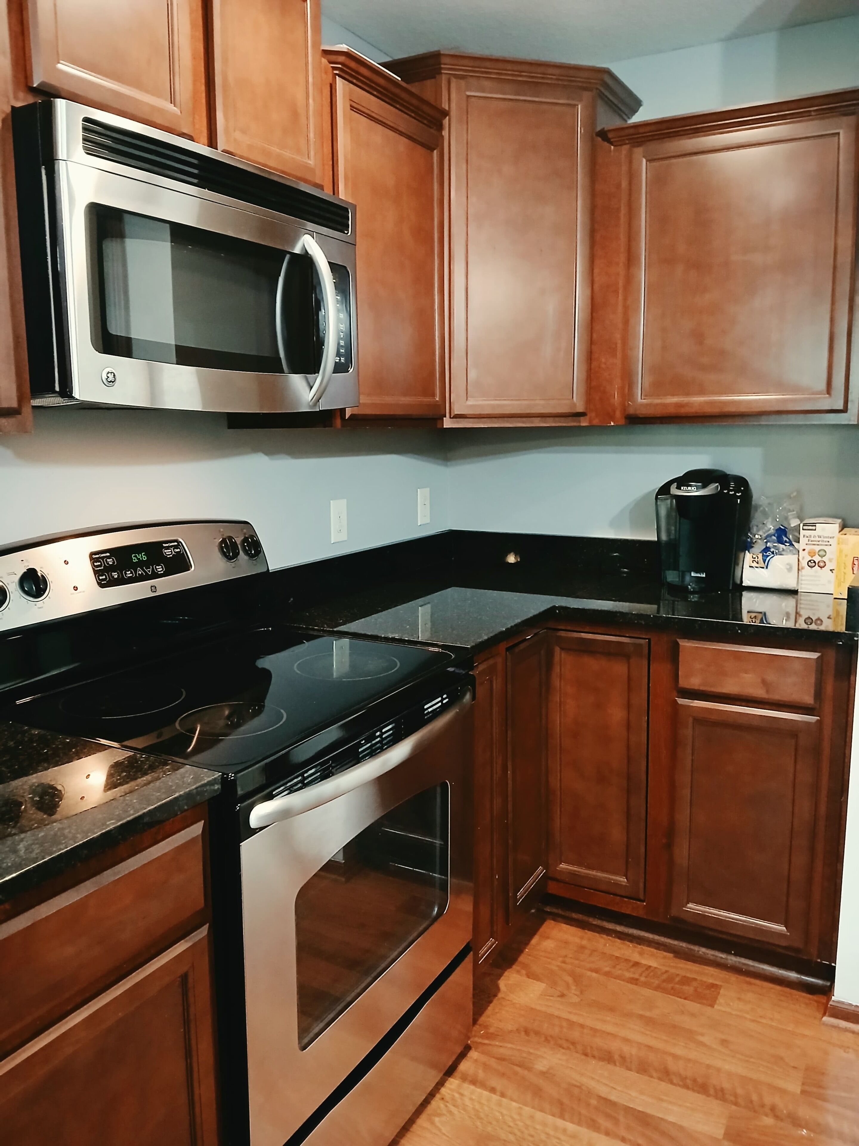 A kitchen with wooden cabinets, a stainless steel microwave, a black stove, and a coffee maker.