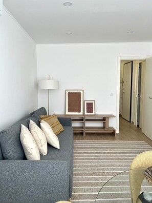 Ein modernes Wohnzimmer mit grauem Sofa, einer Stehlampe, gerahmten Bildern und einer Holzbank.