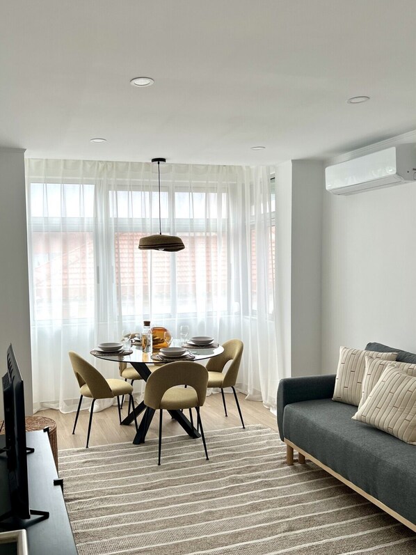 A dining area with a table set for four, a sofa, and a TV on a stand. - Contemporary Living in Amadora (Amadora)