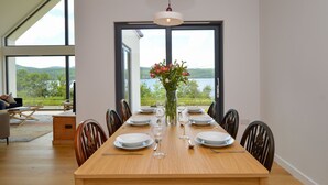 A dining area with a wooden table set for six, large windows, and a view of a lake. - Breathtaking Loch Fyne Escape – Contemporary Home with Incredible Views (Strachur)