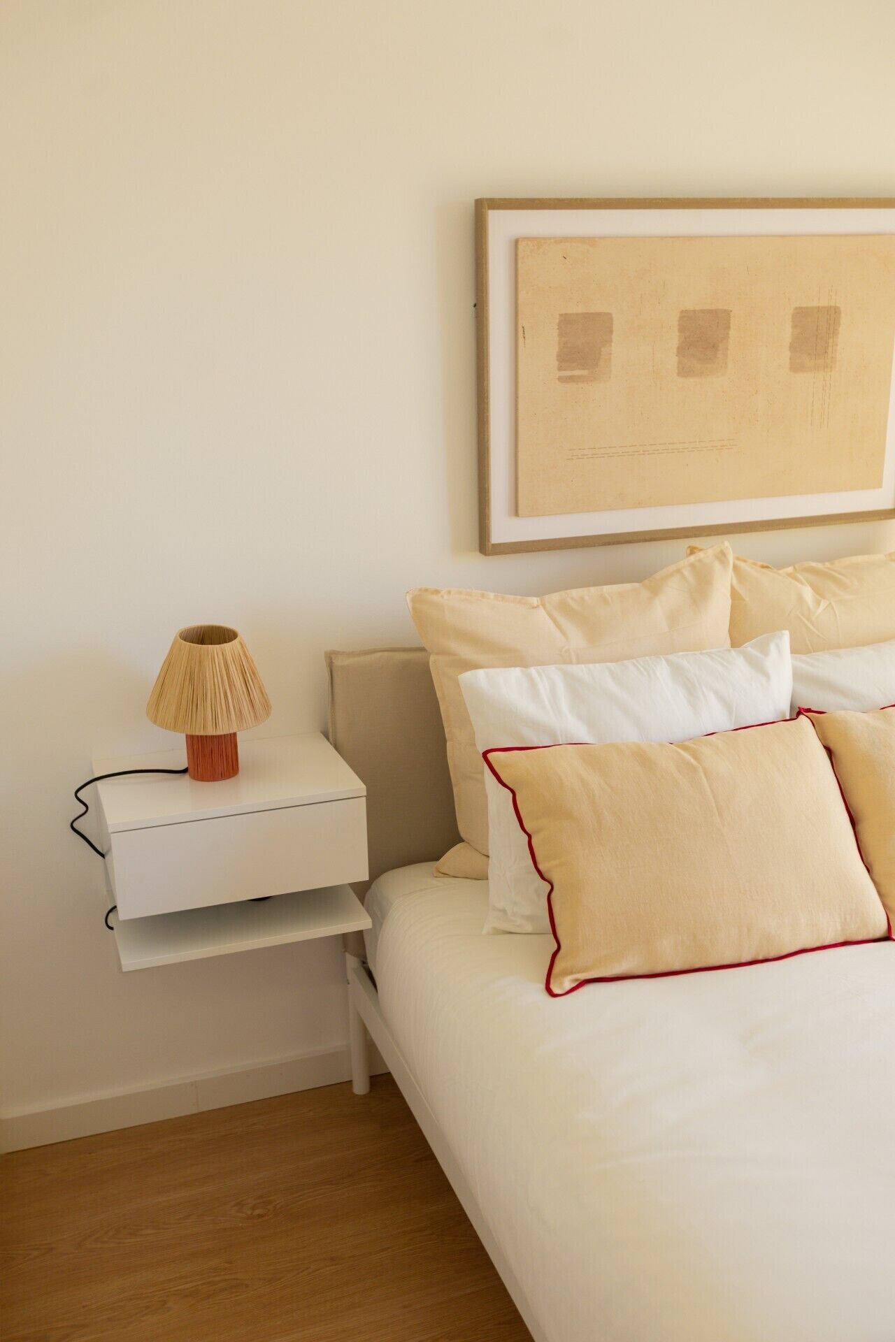 Une chambre à coucher bien rangée, avec un lit, des oreillers, une table de chevet, une lampe et un tableau encadré au mur.