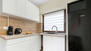 Eine moderne Küche mit weißen Schränken, einem schwarzen Kühlschrank, einer Kaffeemaschine und einem Wasserkocher.