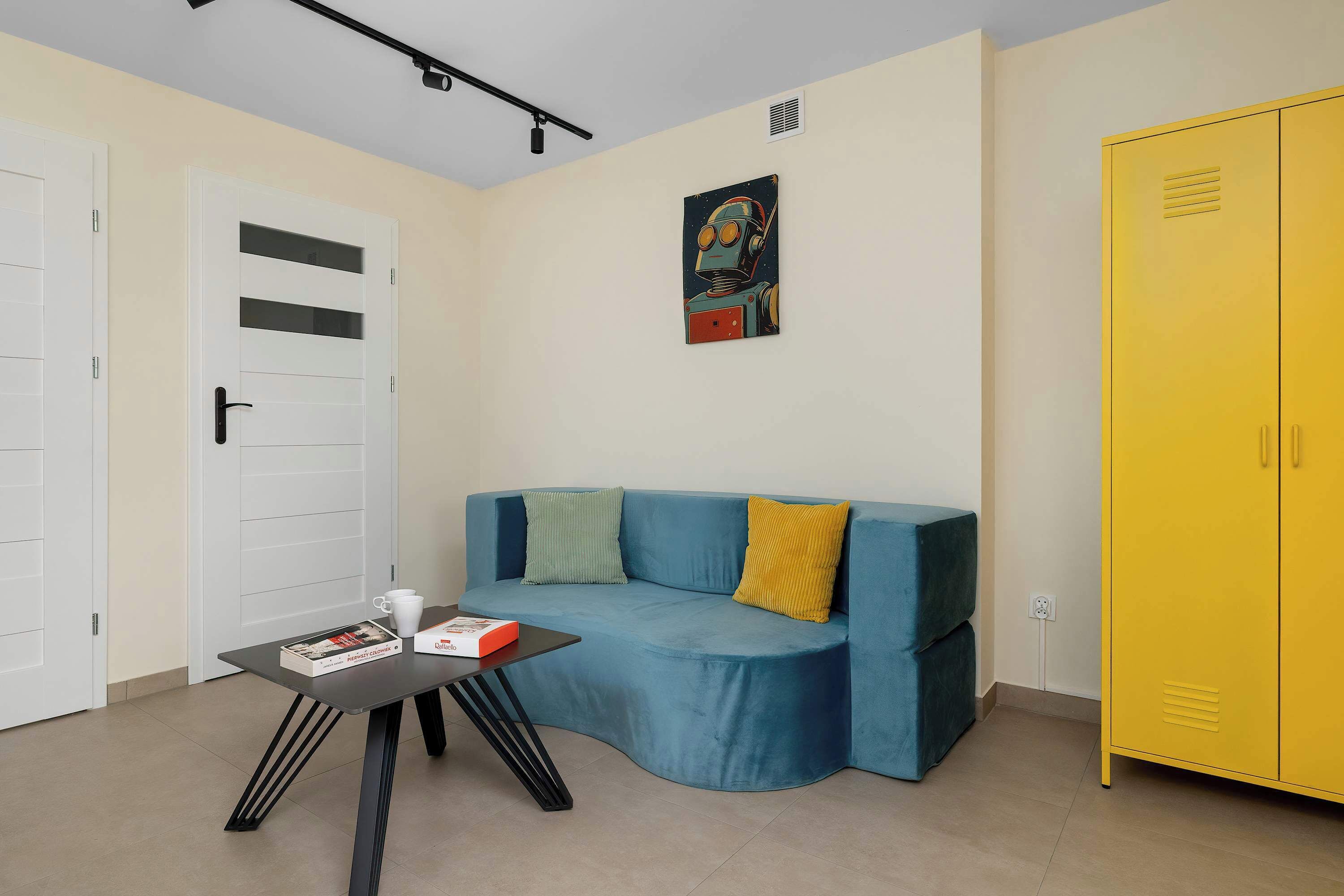 A room with a blue sofa, a yellow wardrobe, a white door, and a painting on the wall.