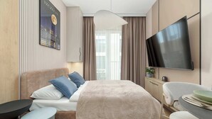 A modern hotel room with a bed, bedside tables, a flat-screen TV, and a view of the outdoors. - Beige Studio with Balcony | By the River (Szczecin)