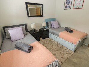A bedroom with two beds, nightstands, a mirror, and wall decorations. - 4 Murrayfields (Newcastle-upon-Tyne)