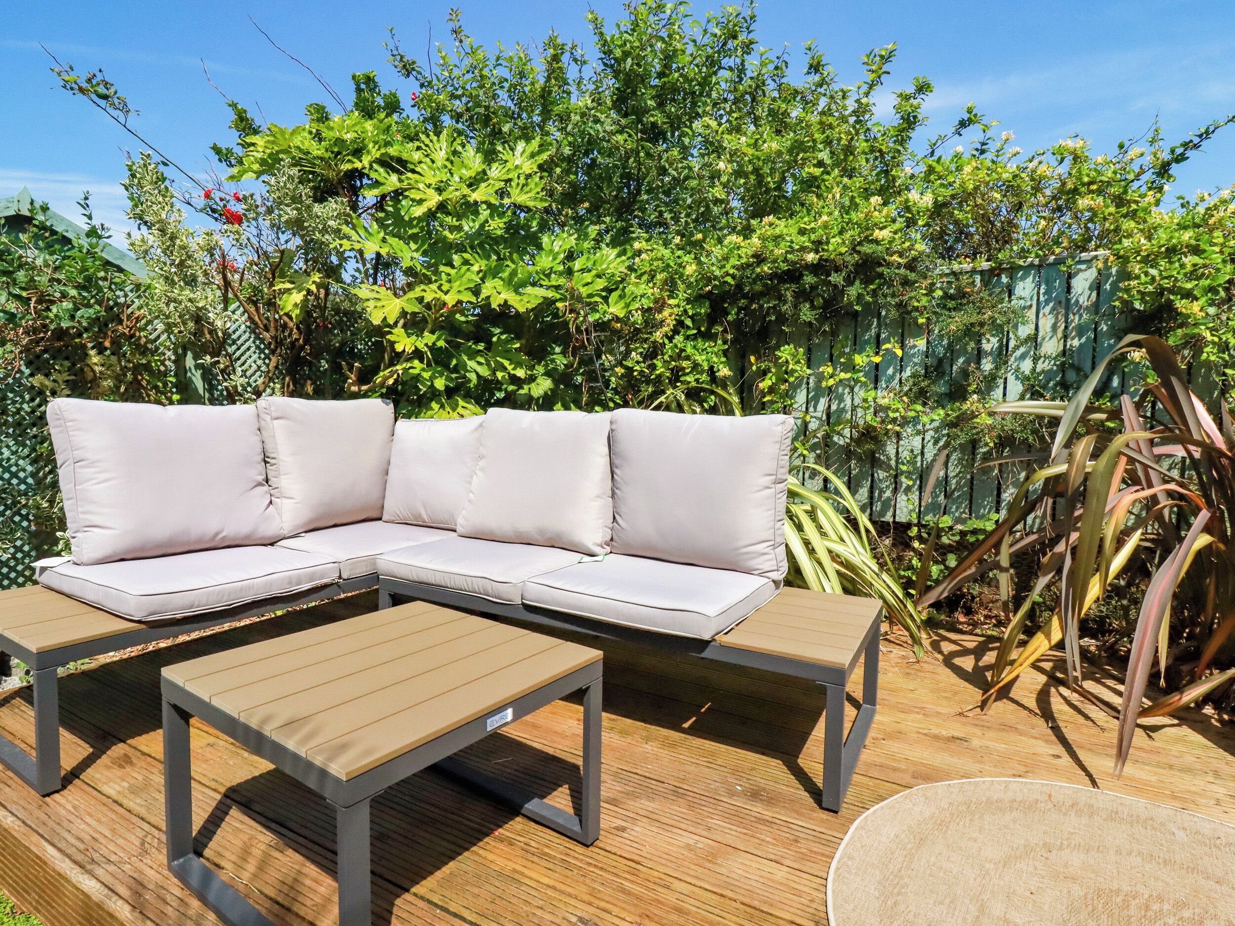 Un canapé modulable avec des coussins et une table basse en bois, le tout placé sur une terrasse en bois.