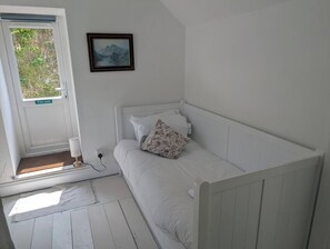 Ein kleines, weißes Zimmer mit einem Einzelbett, einer Flucht-Tür und einem gerahmten Bild an der Wand.