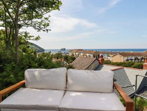 Un balcone con una panca imbottita bianca, con vista su una cittadina costiera con case e il mare.