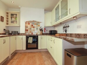 A kitchen with white cabinets, a microwave, a toaster, and a tiled backsplash. - Fairsands (Redruth)