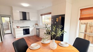 Una cocina moderna con armarios blancos, una estufa y un refrigerador. Hay una mesa de comedor con sillas y un florero con plantas.