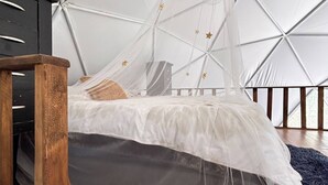 Une pièce dotée d’un plafond aux motifs géométriques, d’un lit surmonté d’un dais en tissu léger et d’une table en bois.