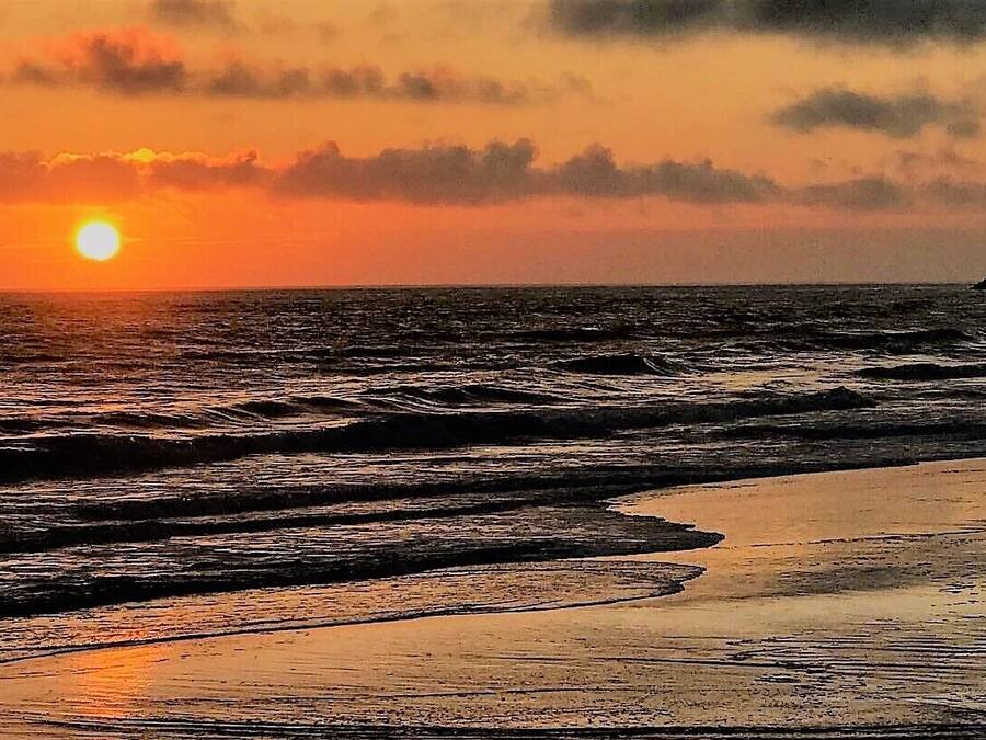 Una playa con olas, una persona caminando y un atardecer.