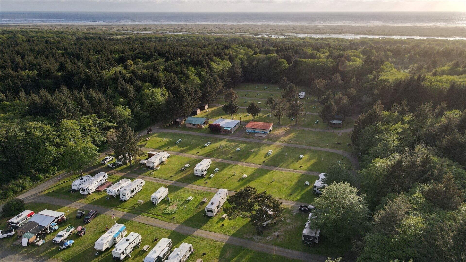 Luchtbeeld van een camping met campers, een klein gebouw en een bebost gebied.