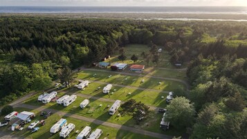 Vista aérea de un camping con vehículos recreativos, un edificio pequeño y un área boscosa.
