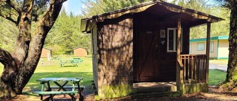 A small wooden cabin with a porch, a picnic table, and a bench nearby.