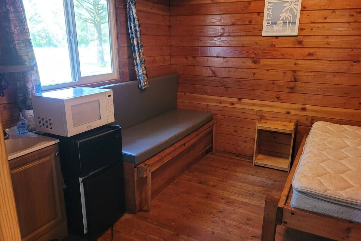 A cabin interior with a wooden bench, a small table, a microwave, a sink, and a bed.