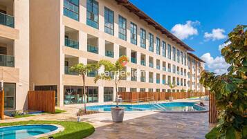A hotel with a swimming pool, outdoor seating, and a large building with multiple windows.