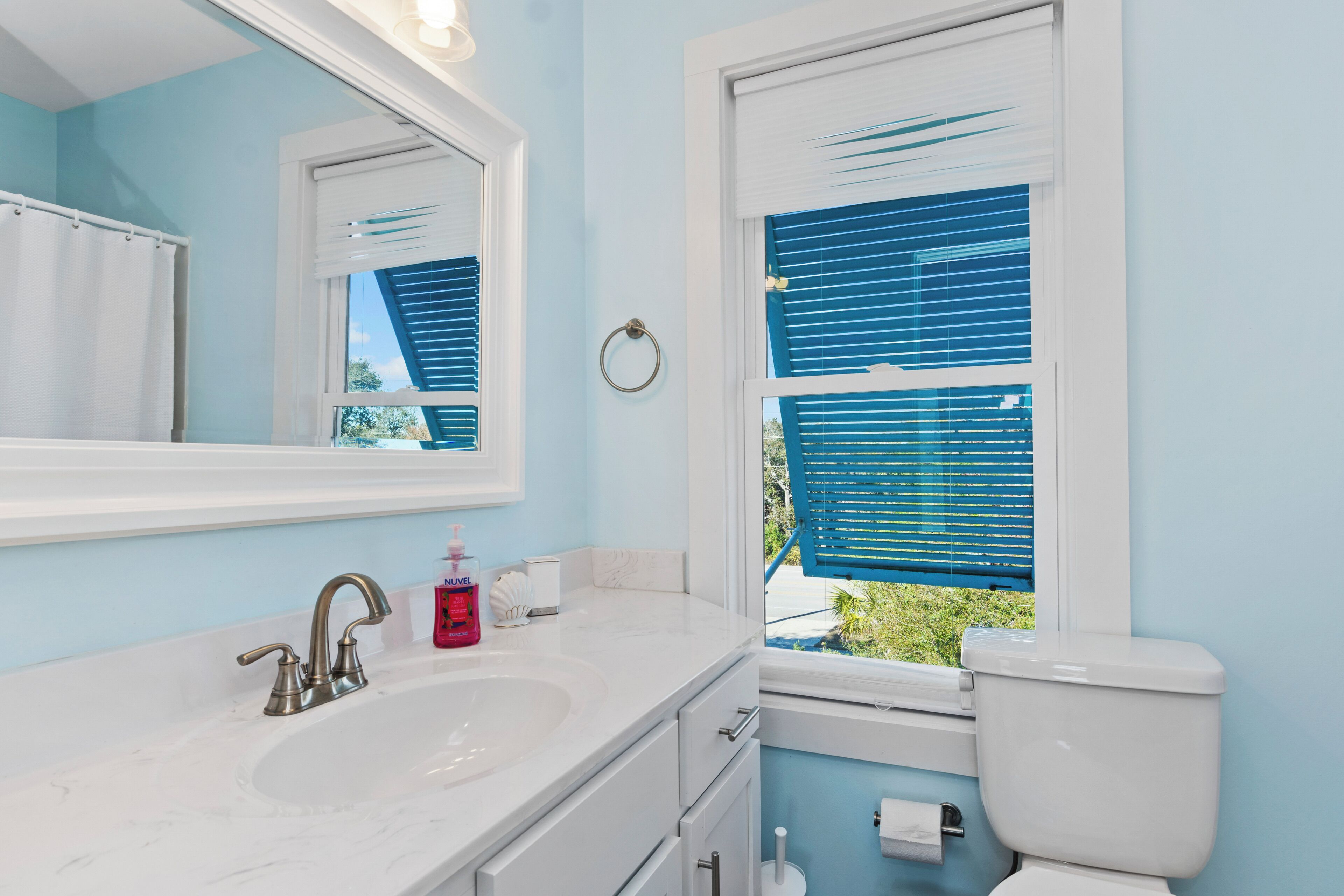 A bathroom with a sink, mirror, toilet, and window with blinds.