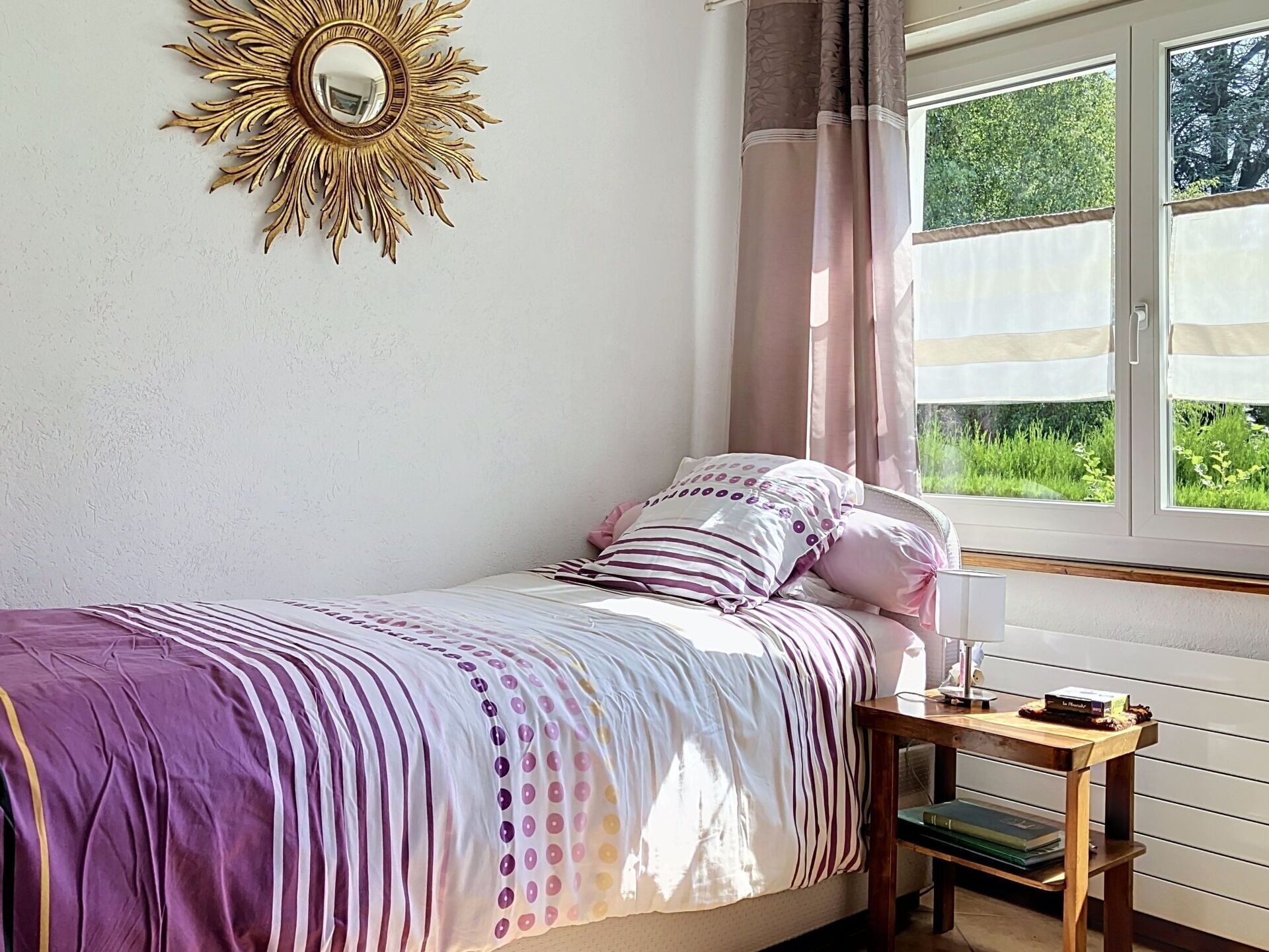 Une chambre à coucher avec un lit, une table de chevet, une fenêtre avec des rideaux et un élément décoratif mural.