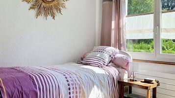 Une chambre à coucher avec un lit, une table de chevet, une fenêtre avec des rideaux et un élément décoratif mural.