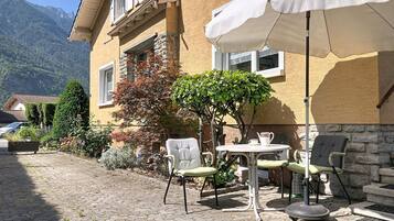 Une terrasse avec des sièges d’extérieur, une table et un parasol blanc.