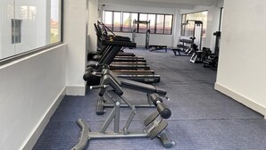 Uma academia com equipamentos de exercício, amplas janelas e piso coberto de carpete.