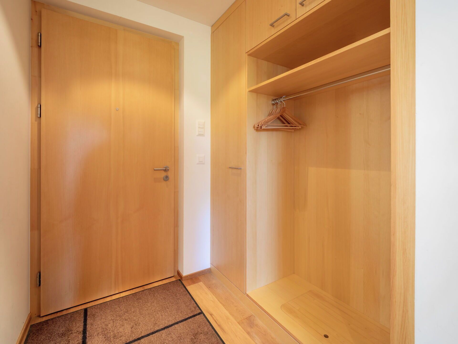Un armario de madera con barra para colgar, una puerta y un estante pequeño.