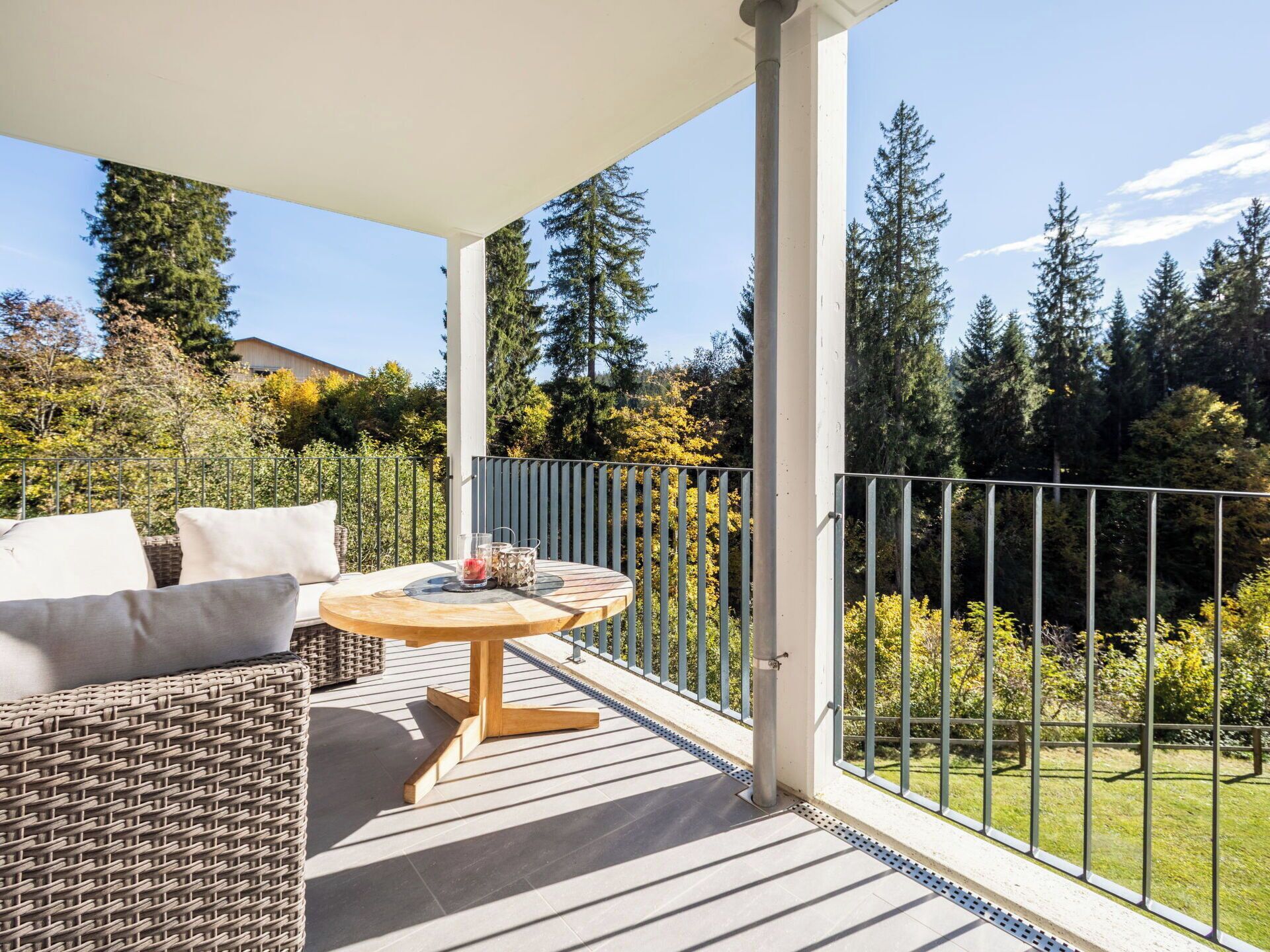 A covered balcony with a wicker sofa, a round wooden table, and a metal railing.