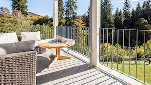 Ein überdachter Balkon mit Rattan-Sofa, einem runden Holztisch und einem Metallgeländer.