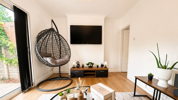 A modern living room with a hanging chair, a TV, a coffee table with books and a remote, and a potted plant.