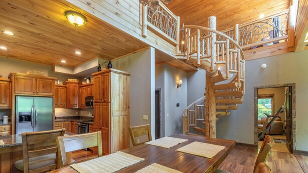 A wooden interior with a spiral staircase, a dining area with a wooden table and chairs, and a kitchen with wooden cabinets and a refrigerator. - Rookery-High-Rollers, Hiking & Hot Tubs–Ultimate Motorcycle-Friendly Retreat! (Whittier)