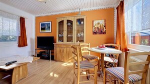 Una habitación con una mesa de comedor de madera, sillas, un televisor, un aparador con puertas de cristal y una ventana con cortinas.