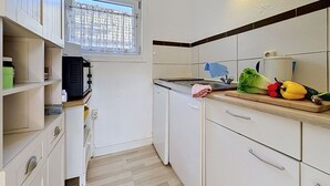 Una cocina compacta con armarios blancos, una ventana con cortina, un lavamanos y una encimera con verduras.