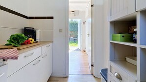 Cocina estrecha con armarios blancos, encimera de madera y vistas a un jardín a través de un ventanal abierto.