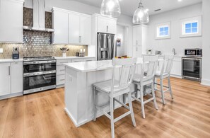 A modern kitchen with white cabinetry, stainless steel appliances, and a central island with bar stools. - Sundance @ St. George Island (Saint George Island)