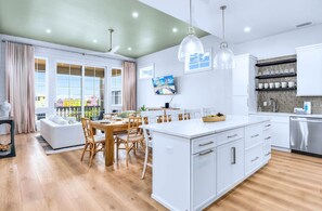 A modern kitchen with white cabinetry, a central island, and a dining area with wooden chairs. - Sundance @ St. George Island (Saint George Island)