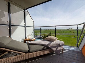 Ein Balkon mit einer Rattan-Couch, einem kleinen Tisch mit einem Buch und einer Tasse sowie Blick auf ein grünes Feld.