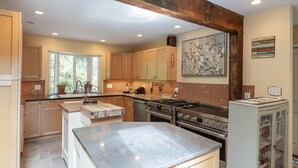 A kitchen with wooden cabinets, a large stove, and a window with a view of greenery. - Rustic & Serene Forest 4 Bedroom Home - West Coast Retreat (Willis Point)
